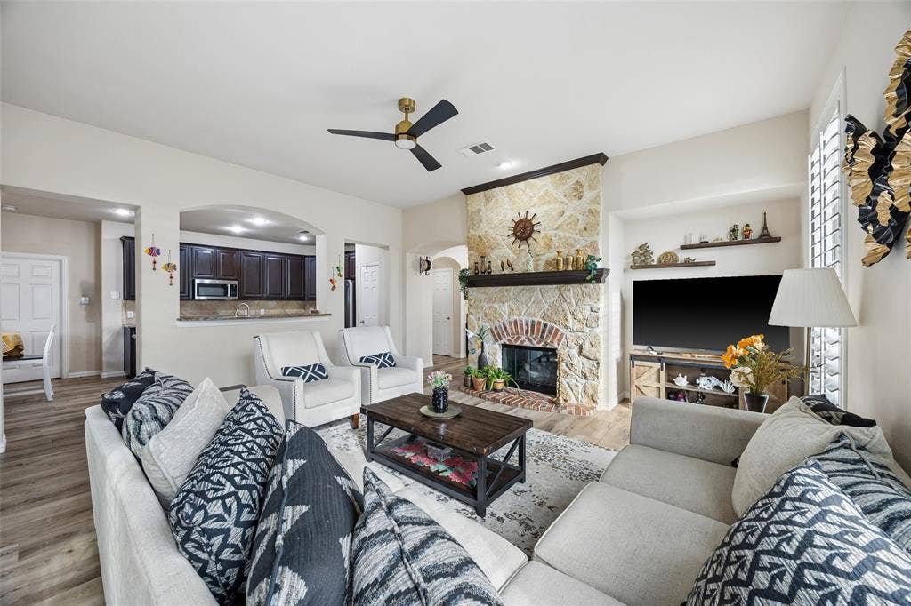 2865 Ridge View Road, Frisco, TX 75034 Stone-clad fireplace with brick interior and wood mantel, wood-finish flooring, ceiling fan, archway, and white plantation shutters