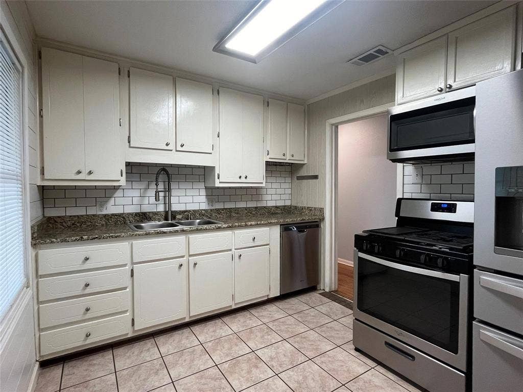 Kitchen featuring white cabinetry, subway tile backsplash, granite-style countertops, stainless steel appliances, and tiled flooring