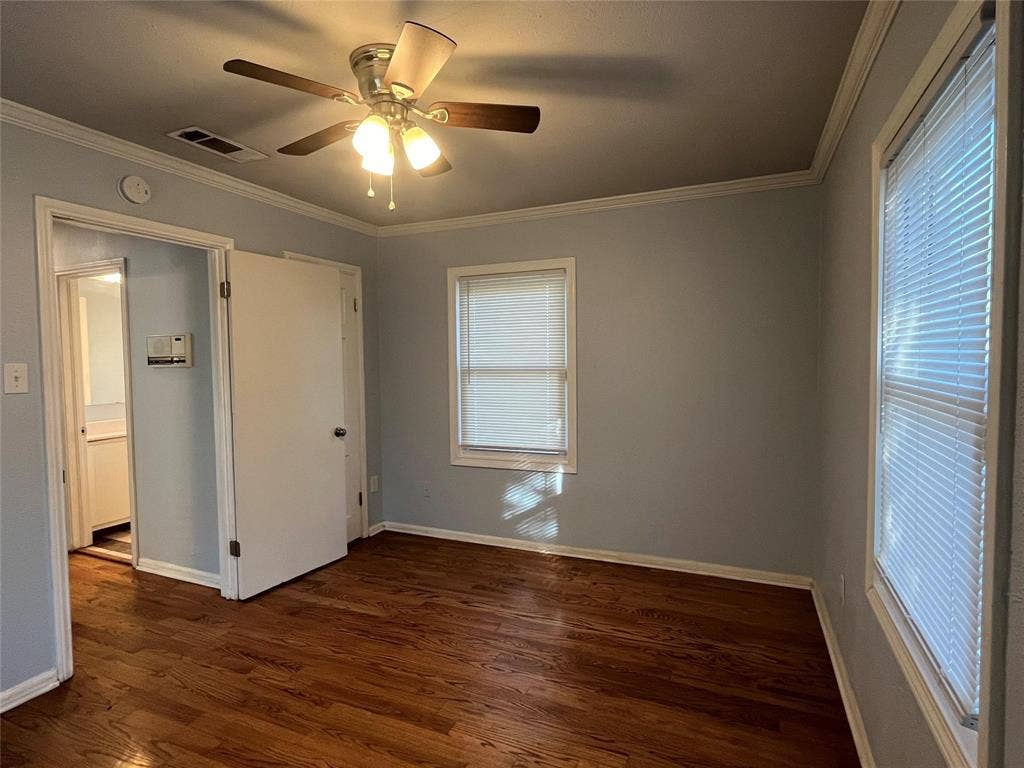 Wood-finish flooring, ceiling fan with integrated lighting, multiple windows with blinds, and painted walls with crown molding