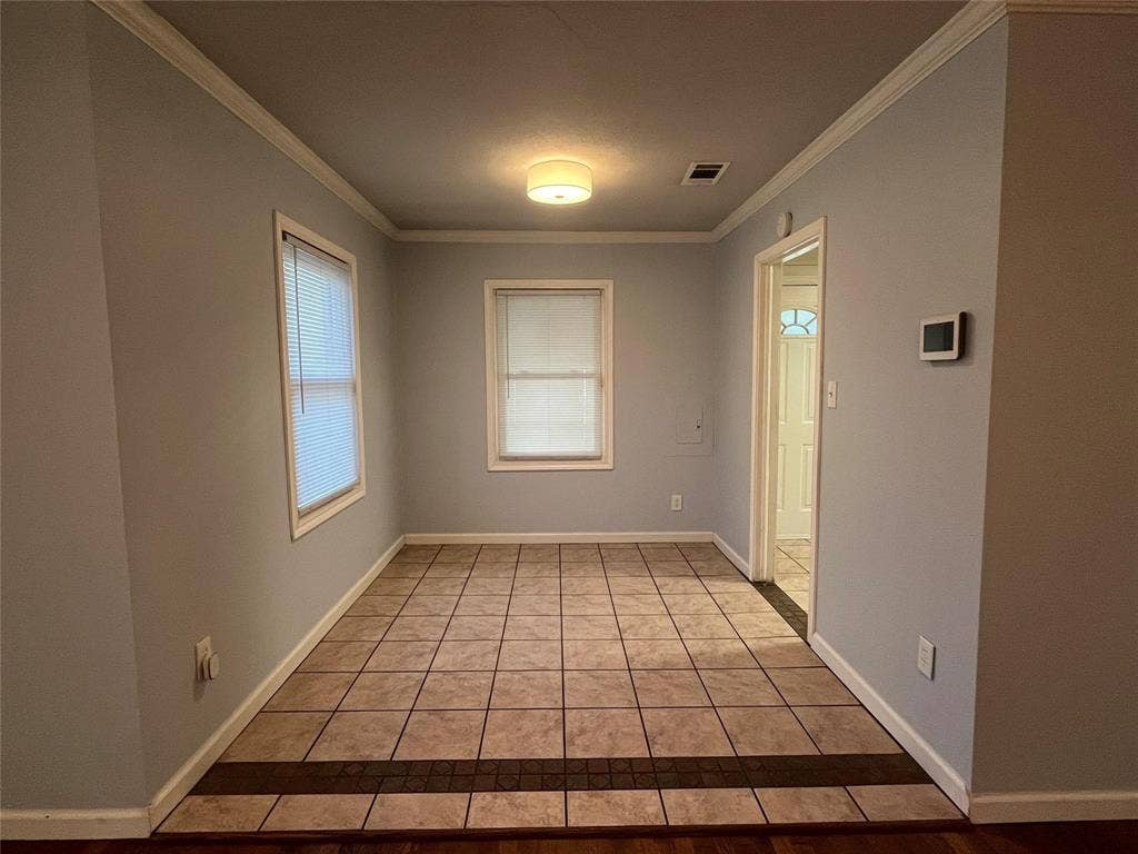 Ceramic tile flooring with a decorative inlay, two windows with blinds, crown molding, and a flush mount ceiling fixture