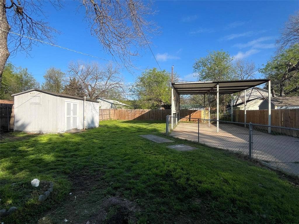 Expansive green space featuring a storage shed, wood fencing, and a covered carport structure