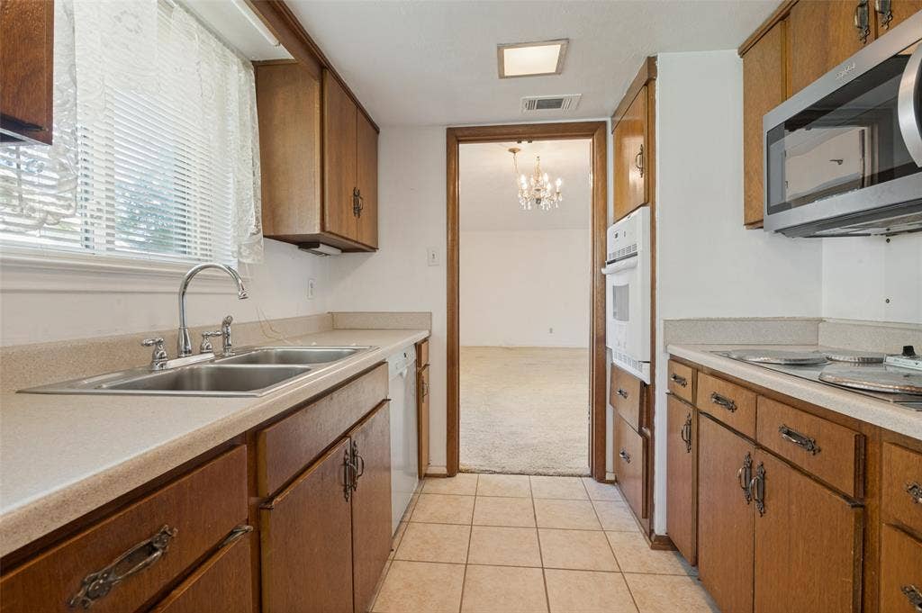 Kitchen featuring wood cabinetry, a double basin stainless steel sink, tile flooring, a built-in oven, and a microwave