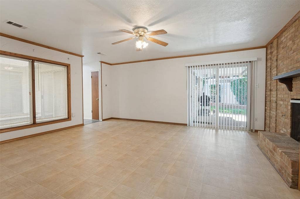 Spacious room featuring tile flooring, a brick fireplace, a ceiling fan with integrated lighting, and a sliding glass door leading to the exterior