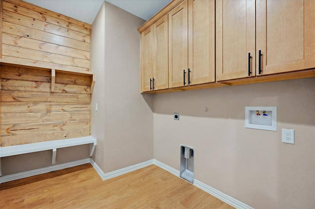 Utility room featuring natural wood-finish flooring, pine plank walls, and custom wood cabinetry with black hardware
