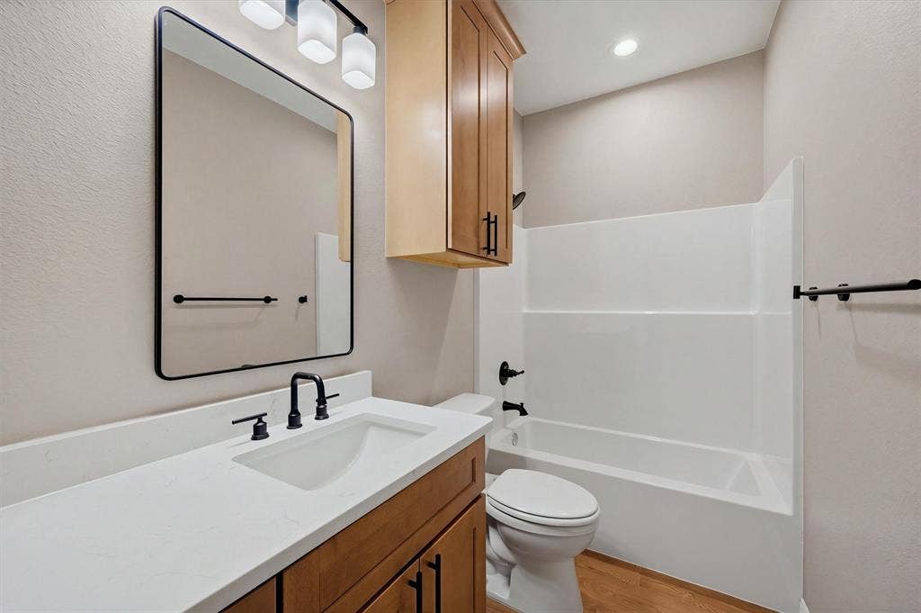 Bathroom featuring a vanity with a light-tone countertop, wood cabinetry, a rectangular mirror with a black frame, matte black hardware, and a tub-shower combination with a white surround
