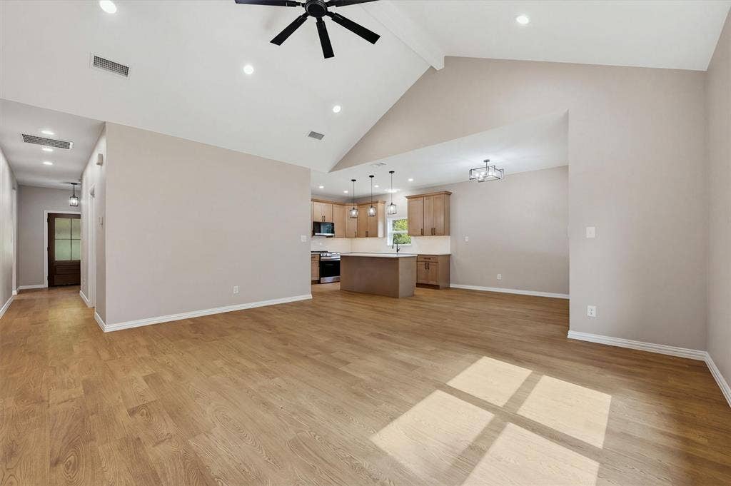 Vaulted ceilings, wood-finish flooring, recessed lighting, ceiling fan, and built-in kitchen cabinetry with a central island