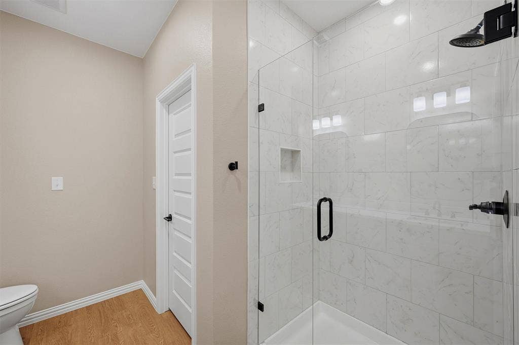 Walk-in shower featuring floor-to-ceiling tile surround, a built-in recessed niche, a frameless glass door, and matte black plumbing fixtures