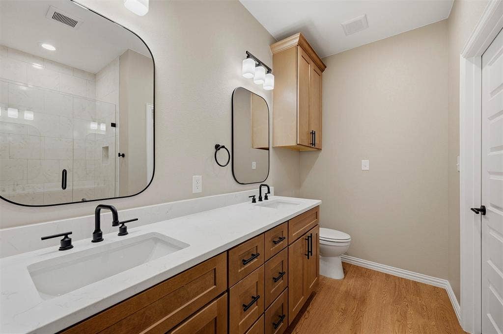 Double vanity with rectangular undermount sinks, stone countertops, wood-finish cabinetry, matte black fixtures, and custom rounded-corner mirrors