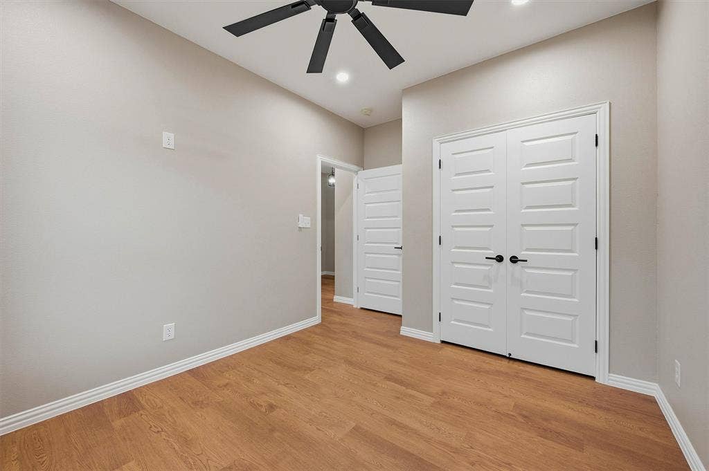 Wood-finish flooring, double-panel closet doors with matte black hardware, recessed lighting, and a multi-blade ceiling fan