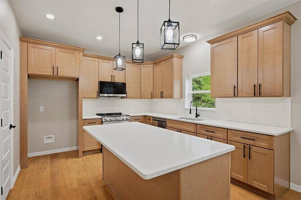 Kitchen featuring light wood-finish cabinetry, white solid-surface countertops, subway tile backsplash, a center island, and black geometric pendant lighting