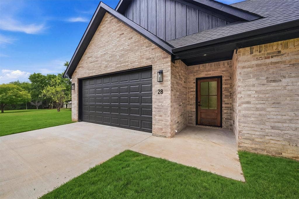 Exterior facade featuring light-toned brick masonry, dark metal gabled roofing, a multi-panel garage door, and a wood entry door with glass paneling