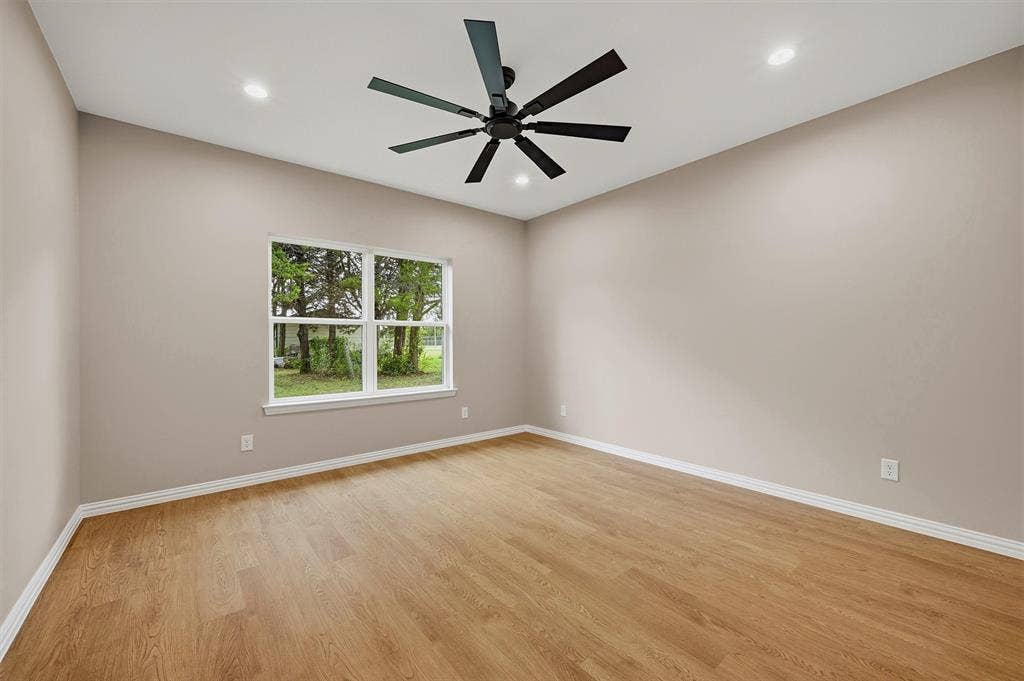Neutral-toned interior room featuring wood-finish flooring, recessed lighting, and a matte black ceiling fan