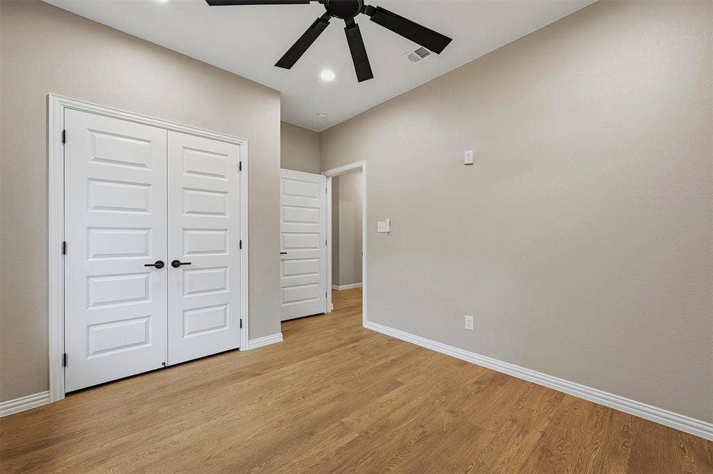 Wood-finish flooring, neutral wall tones, multi-panel doors with matte black hardware, and a ceiling-mounted fan with integrated lighting