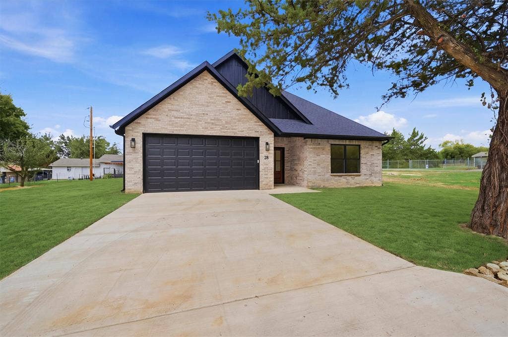 Single-story residence featuring light-toned masonry siding, a dark-toned gable roof, an attached two-car garage, and a concrete driveway