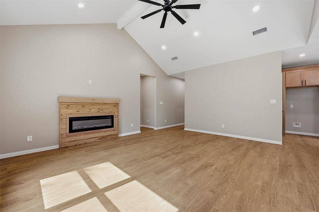Vaulted ceilings featuring a central beam and recessed lighting, wood-finish flooring, a wall-mounted electric fireplace with a wood-plank surround, and integrated wooden cabinetry