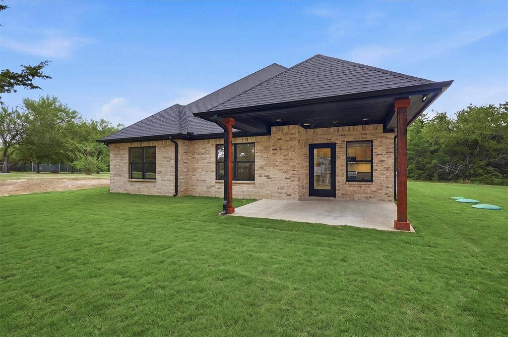 Light-toned brick exterior featuring a covered rear patio, dark-finished wood support posts, a concrete foundation, and a multi-faceted roofline