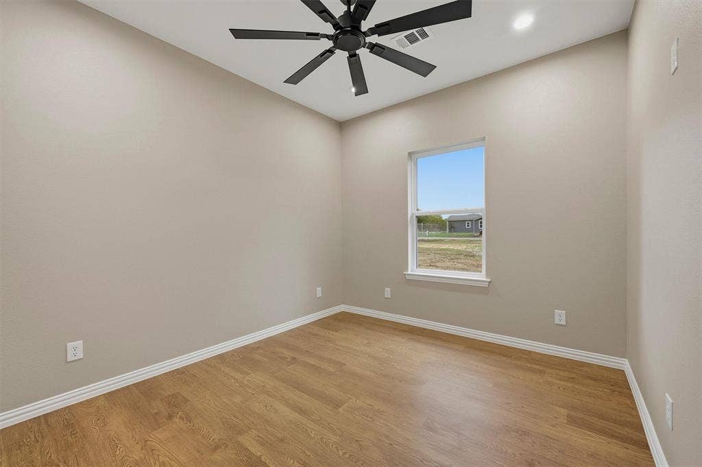 Neutral interior featuring wood-finish flooring, a matte black multi-blade ceiling fan, and a single-pane window with natural light
