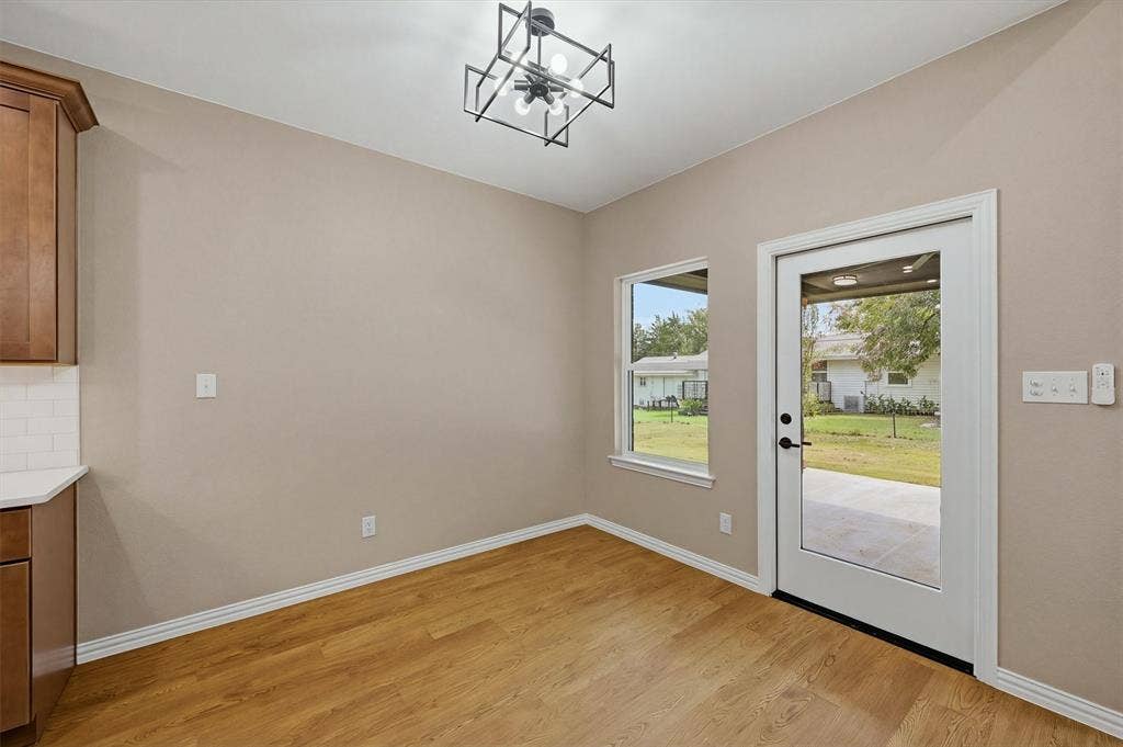 Wood-finish flooring, geometric ceiling light fixture, cabinetry with stone-finish countertops, subway tile backsplash, and glass-paneled exterior door