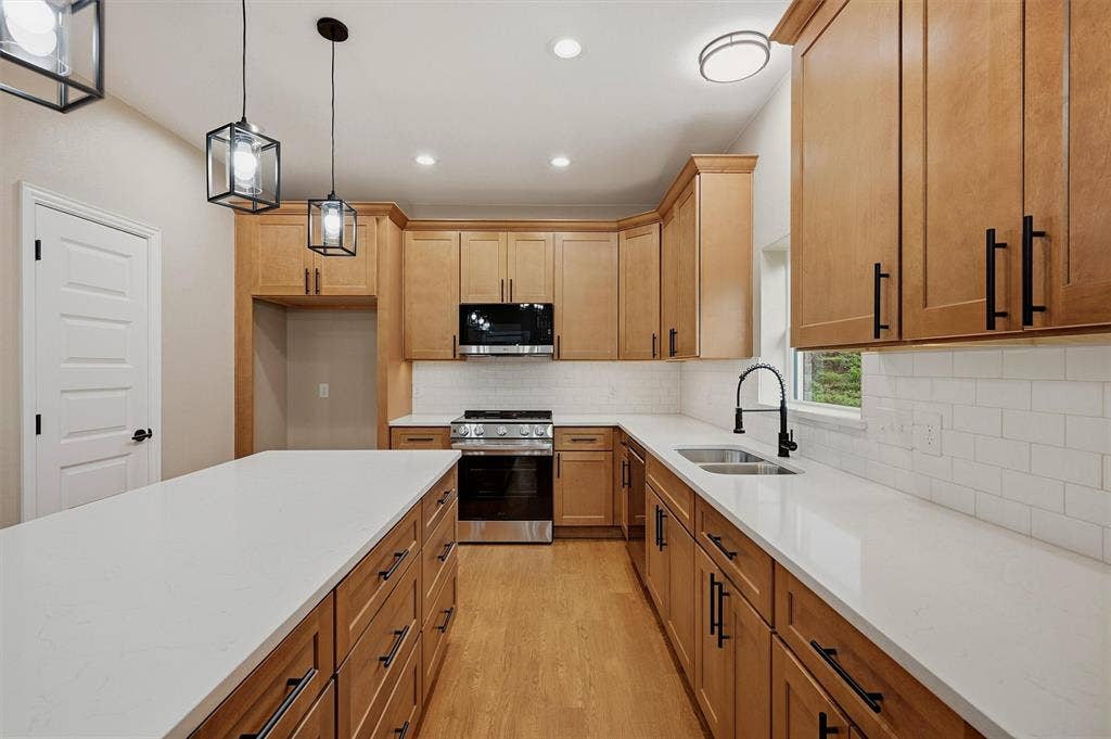 Kitchen featuring wood cabinetry, white stone-finish countertops, subway tile backsplash, stainless steel appliances, and matte black hardware