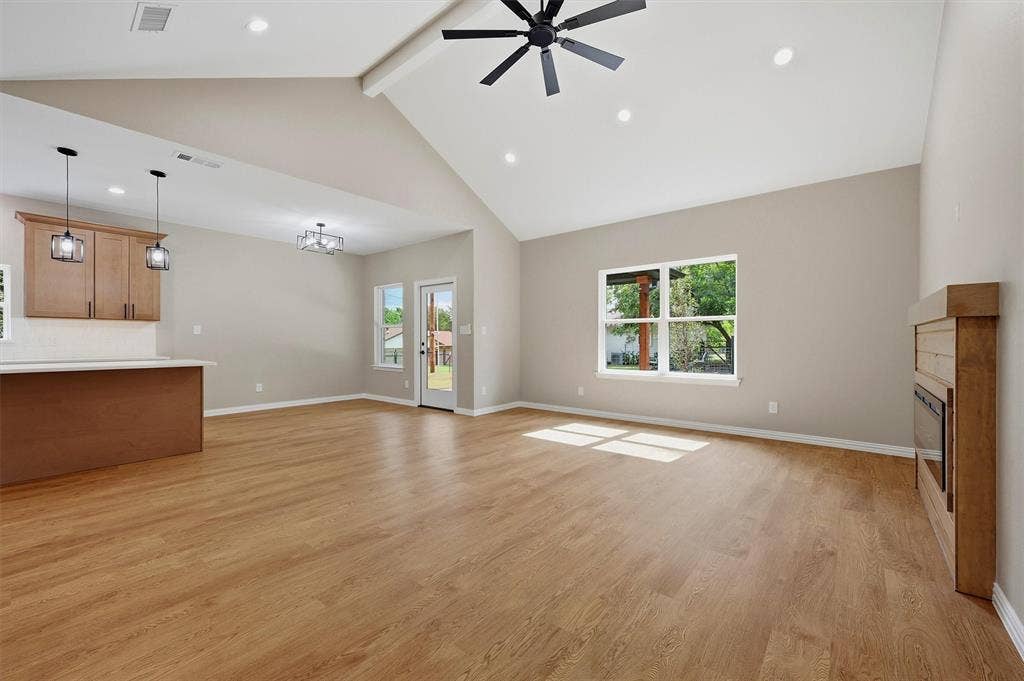 Vaulted ceilings, wood-finish flooring, recessed lighting, floor-to-ceiling fireplace mantel, and kitchen with wood cabinetry