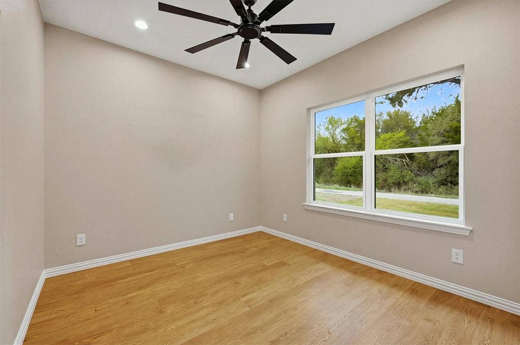 Room featuring wood-finish flooring, recessed lighting, a ceiling fan, and a window with exterior greenery