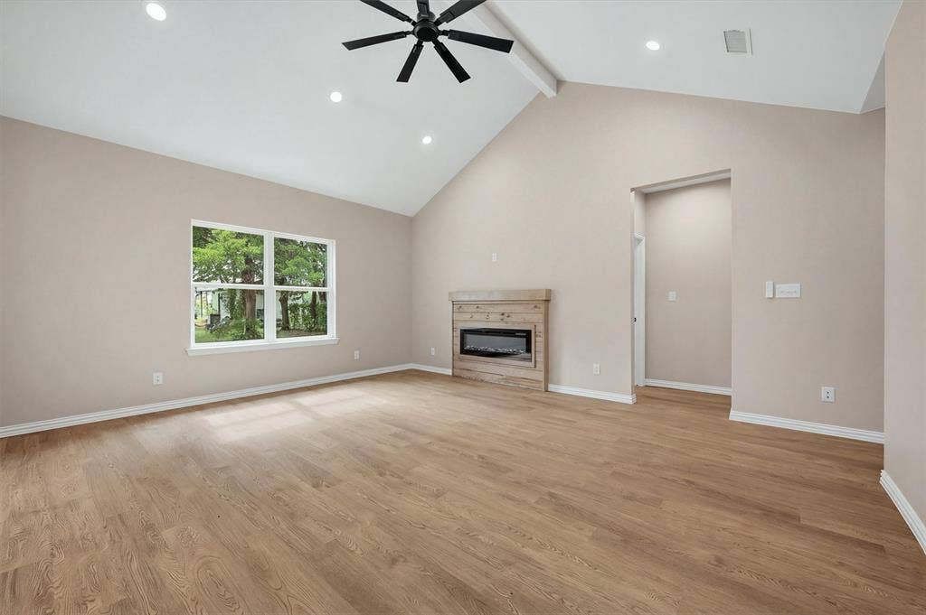 Vaulted ceiling with recessed lighting, wood-finish flooring, and a fireplace featuring a rustic-style wood mantel