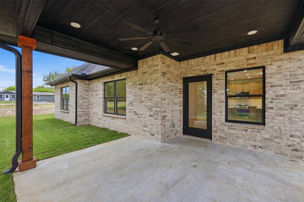Covered outdoor patio featuring a dark wood-paneled ceiling, recessed lighting, a ceiling fan, and stained wood support posts, complemented by a light brick exterior finish
