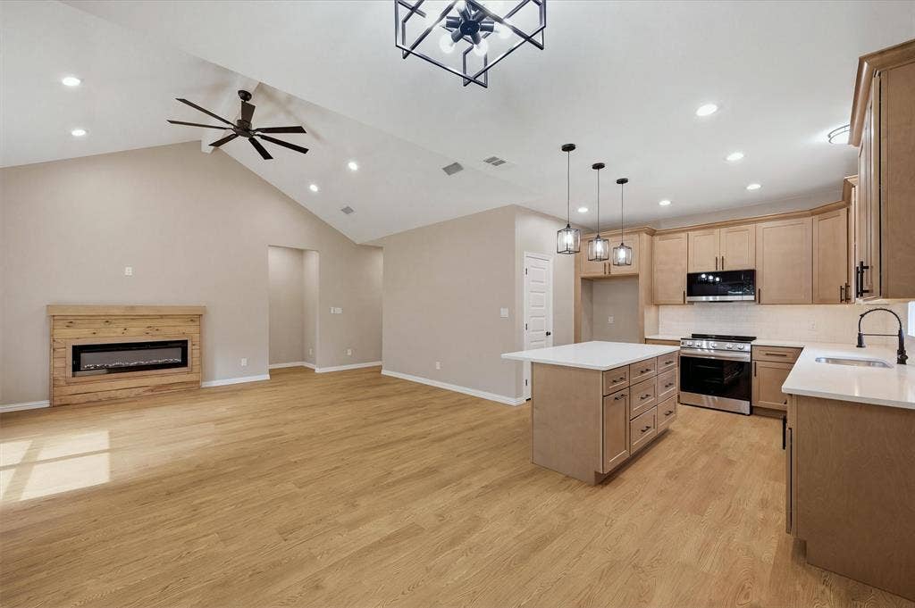 Open-concept kitchen featuring wood-finish cabinetry, stone-surface countertops, and an integrated center island with pendant lighting