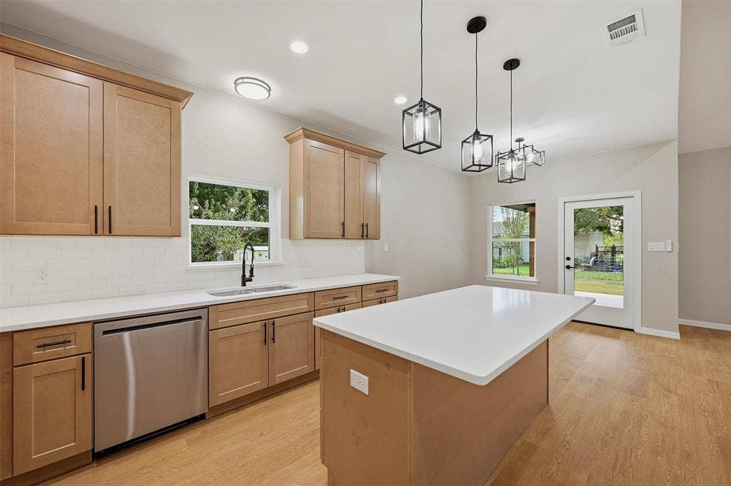 Kitchen featuring shaker-style cabinetry, white countertops, stainless steel dishwasher, geometric pendant lighting, and wood-finish flooring