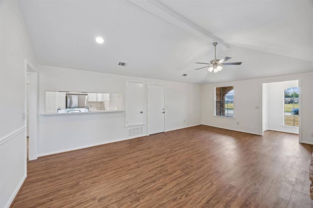 1613 19th Street, Plano, TX 75074 Vaulted ceiling with exposed beam, wood-finish flooring, ceiling fan with integrated lighting, pass-through window to kitchen, and arched doorway