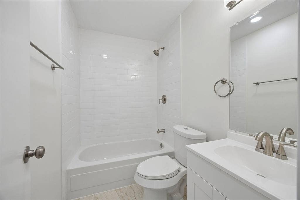 1613 19th Street, Plano, TX 75074 Clean, updated bathroom featuring a white subway tile surround with integrated tub-shower combination, white vanity with rectangular sink, brushed nickel fixtures, recessed ceiling lighting, and wood-finish flooring