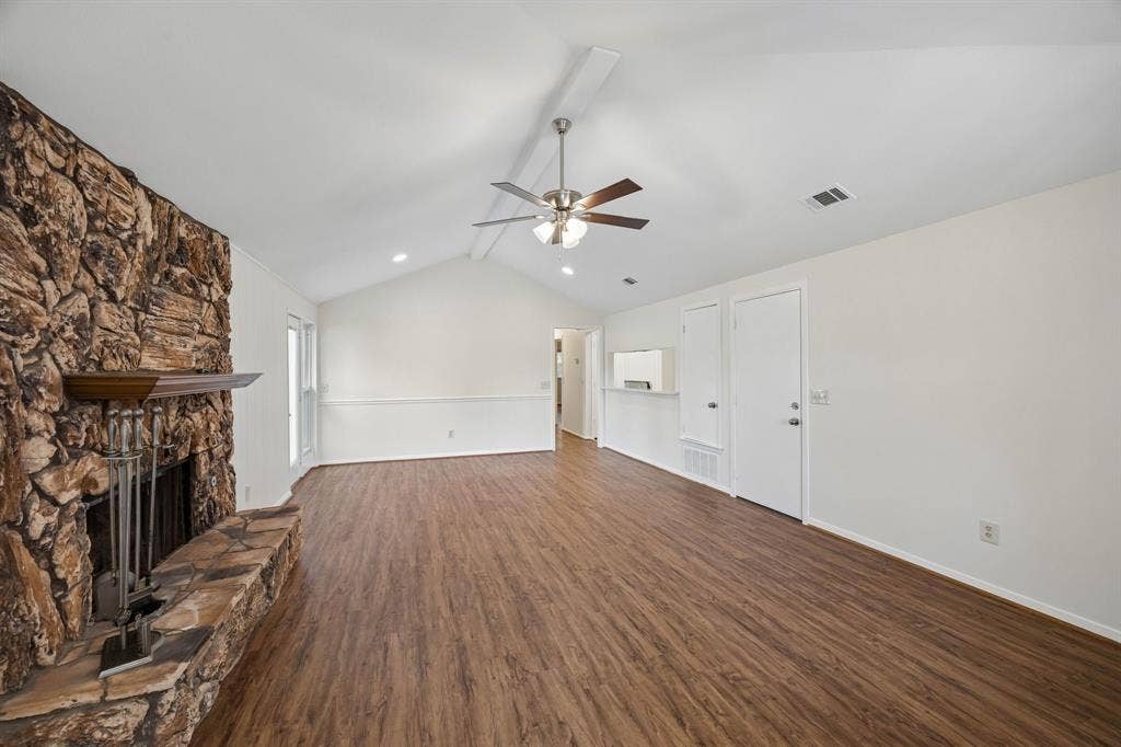 1613 19th Street, Plano, TX 75074 Spacious room featuring a stone fireplace with hearth, wood-finish flooring, vaulted ceilings, and a ceiling fan