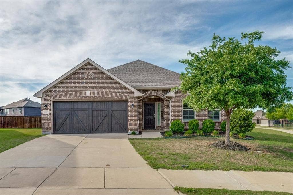 6229 Gloucester Drive, Celina, TX 76227 Brick exterior with a gabled roofline, arched entry, decorative garage door, and established landscaping