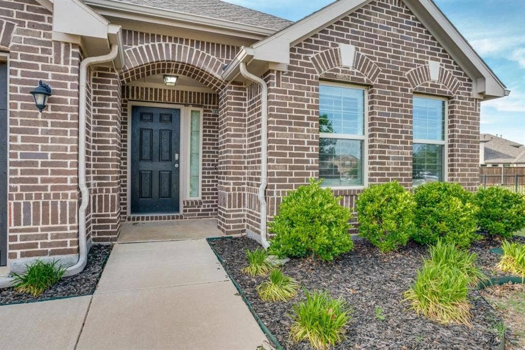 6229 Gloucester Drive, Celina, TX 76227 Brick exterior with architectural accent arches, an arched entry, a dark paneled door, and front landscaping