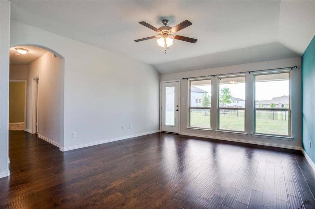 6229 Gloucester Drive, Celina, TX 76227 Dark wood-finish flooring, vaulted ceiling, built-in ceiling fan with light fixture, three large windows, and an arched entryway