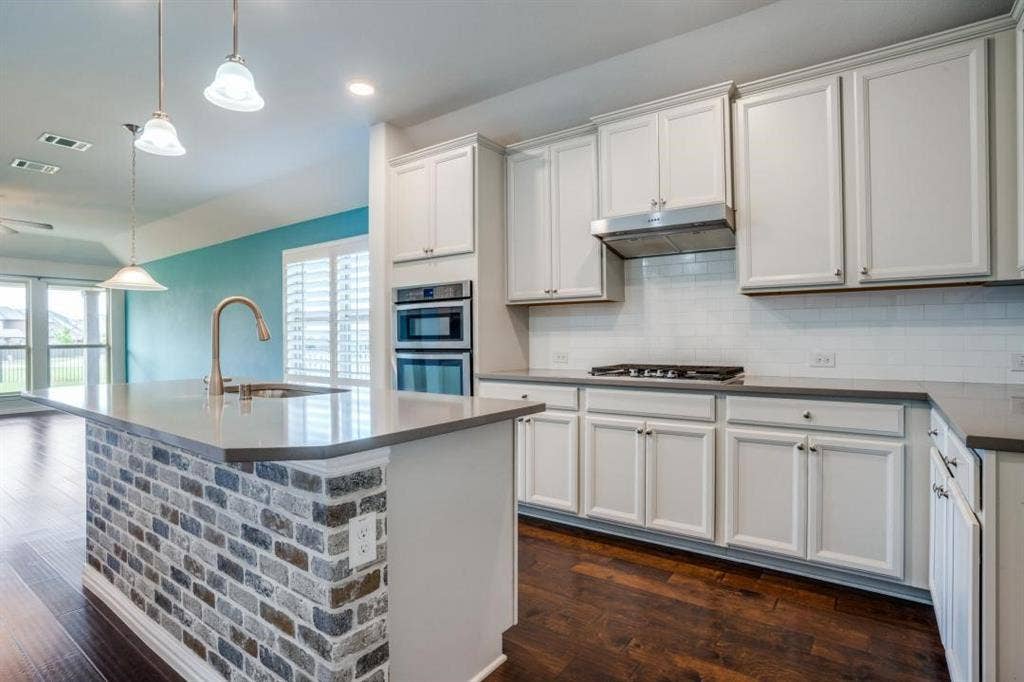 6229 Gloucester Drive, Celina, TX 76227 Kitchen featuring white cabinetry, built-in double ovens, a gas range with range hood, a tiled backsplash, and a kitchen island with a brick finish and integrated sink