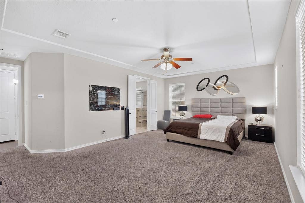 Tray ceiling with crown molding, ceiling fan, carpeted flooring, and a window with blinds