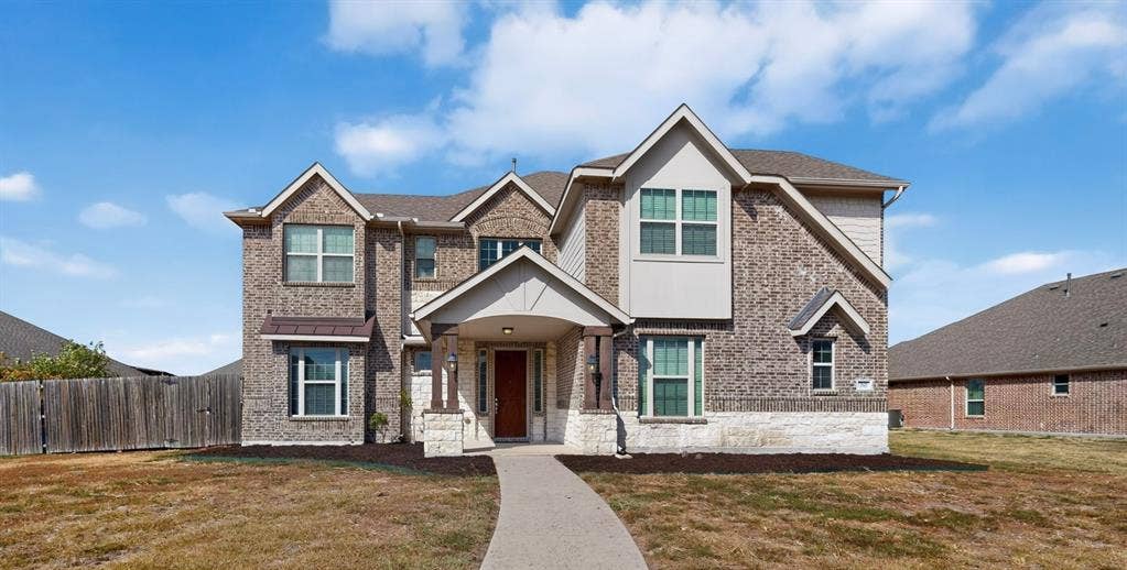 Two-story residence featuring a brick and stone exterior, gabled rooflines, a covered entry, and a paved walkway