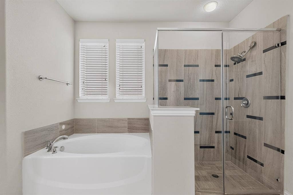Soaking tub with a tiled surround, dual windows, and a separate glass-enclosed shower featuring patterned tile