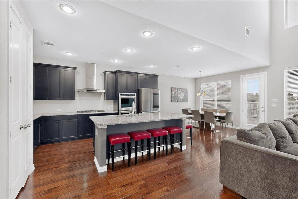 Open-concept living area featuring wood-finish flooring, a kitchen island with stone countertop, stainless steel appliances, and high ceilings