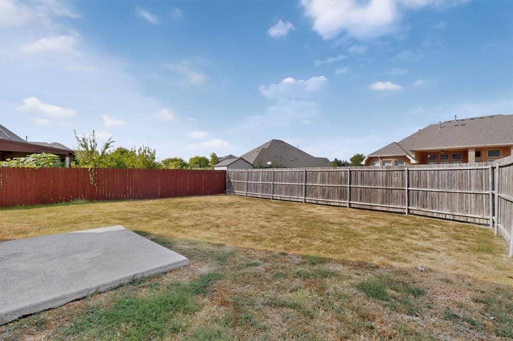 Expansive backyard with a concrete pad, surrounded by a wood privacy fence