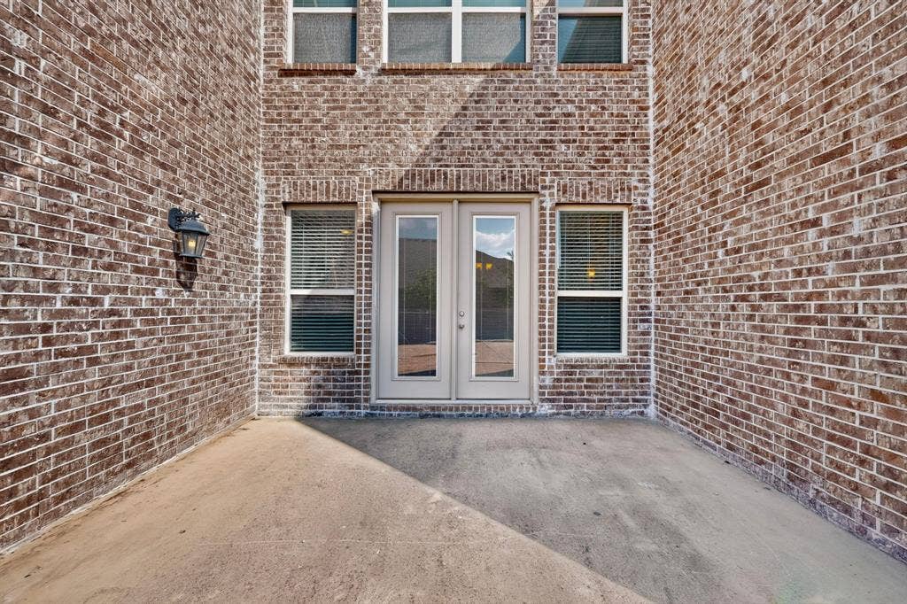 Brick exterior with a concrete patio, double French doors, and an exterior wall light fixture