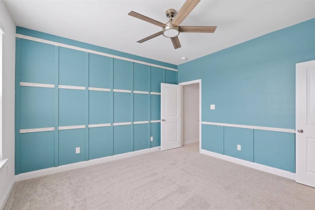 Accent wall with grid paneling, neutral carpet, ceiling fan with brushed nickel finish, and white paneled doors