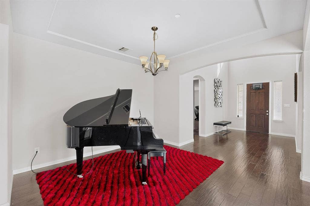 Tray ceiling with a decorative chandelier, dark wood-finish flooring, and arched entryway