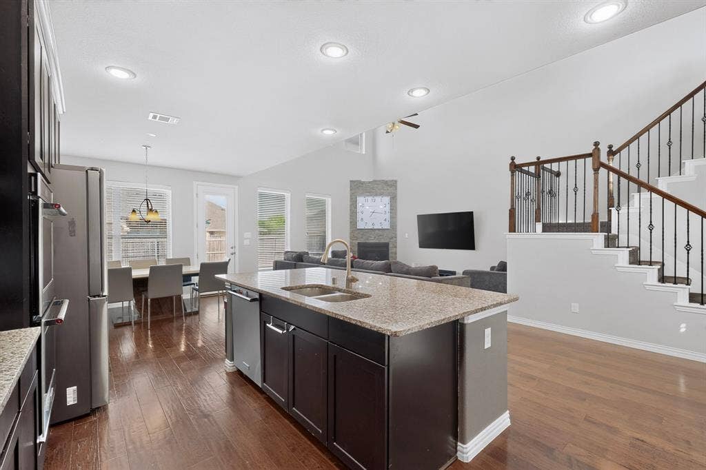 Kitchen island with a granite countertop, stainless steel appliances, wood-finish flooring, vaulted ceilings, and an elegant staircase with wrought iron balusters