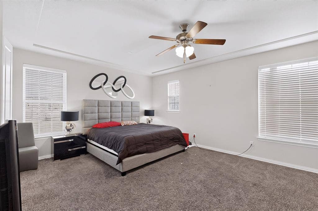 Tray ceiling with crown molding, ceiling fan with integrated lighting, multiple windows with blinds, and carpeted flooring
