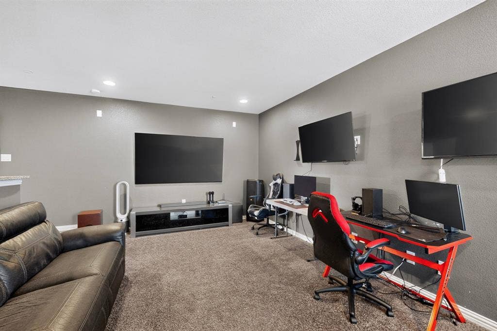 Recessed lighting illuminates a spacious room with wall-mounted televisions and neutral-toned carpeting