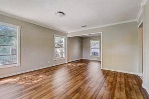 7729 Hillard Drive, Dallas, TX 75217 Bright corner room showcasing gleaming wood-finish flooring throughout, abundant natural light from multiple windows with transom detailing, clean white crown molding, and neutral wall finishes ideal for versatile decorating