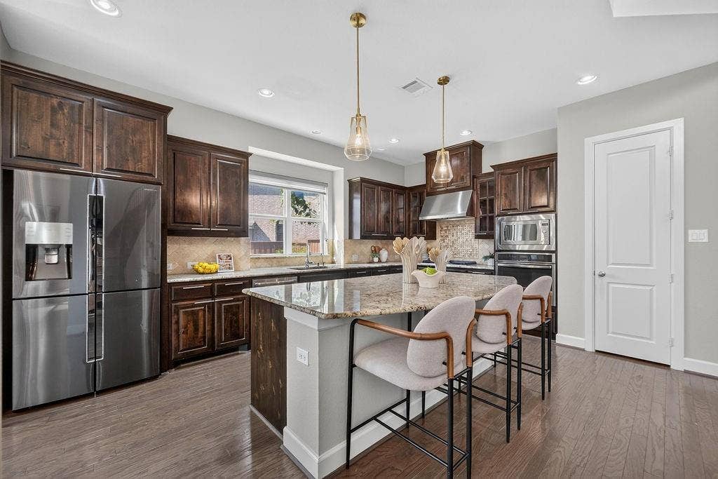 Kitchen featuring dark wood cabinetry, stone-surface countertops, central island, stainless steel built-in appliances, and wood-finish flooring