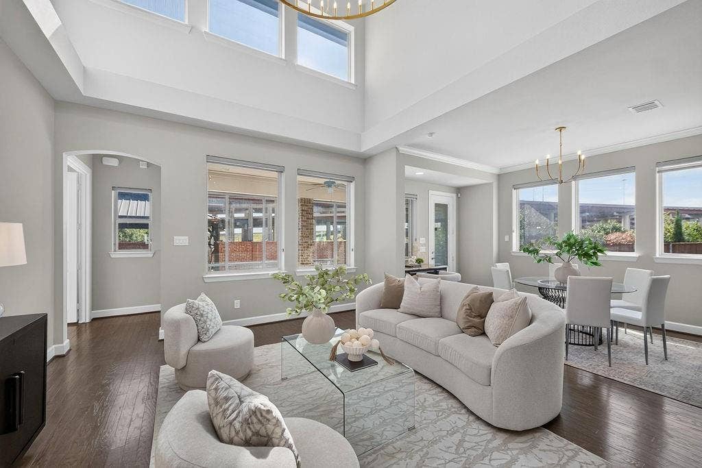 High-ceilinged room featuring wood-finish flooring, large-format windows, and two tiered-arm chandeliers